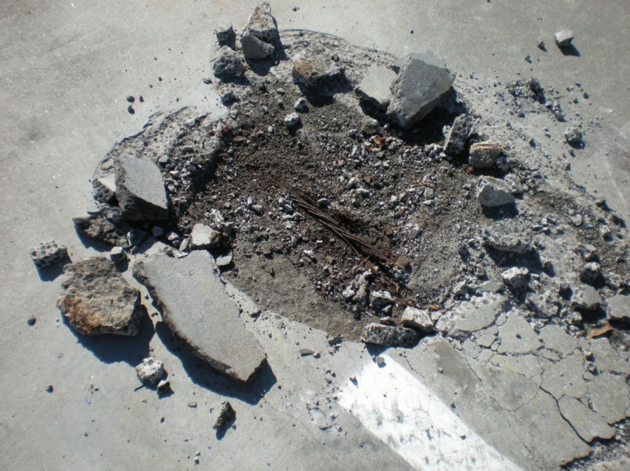 A damaged section of a parking garage floor showing an exposed and corroded steel tendon within a concrete post tension slab.